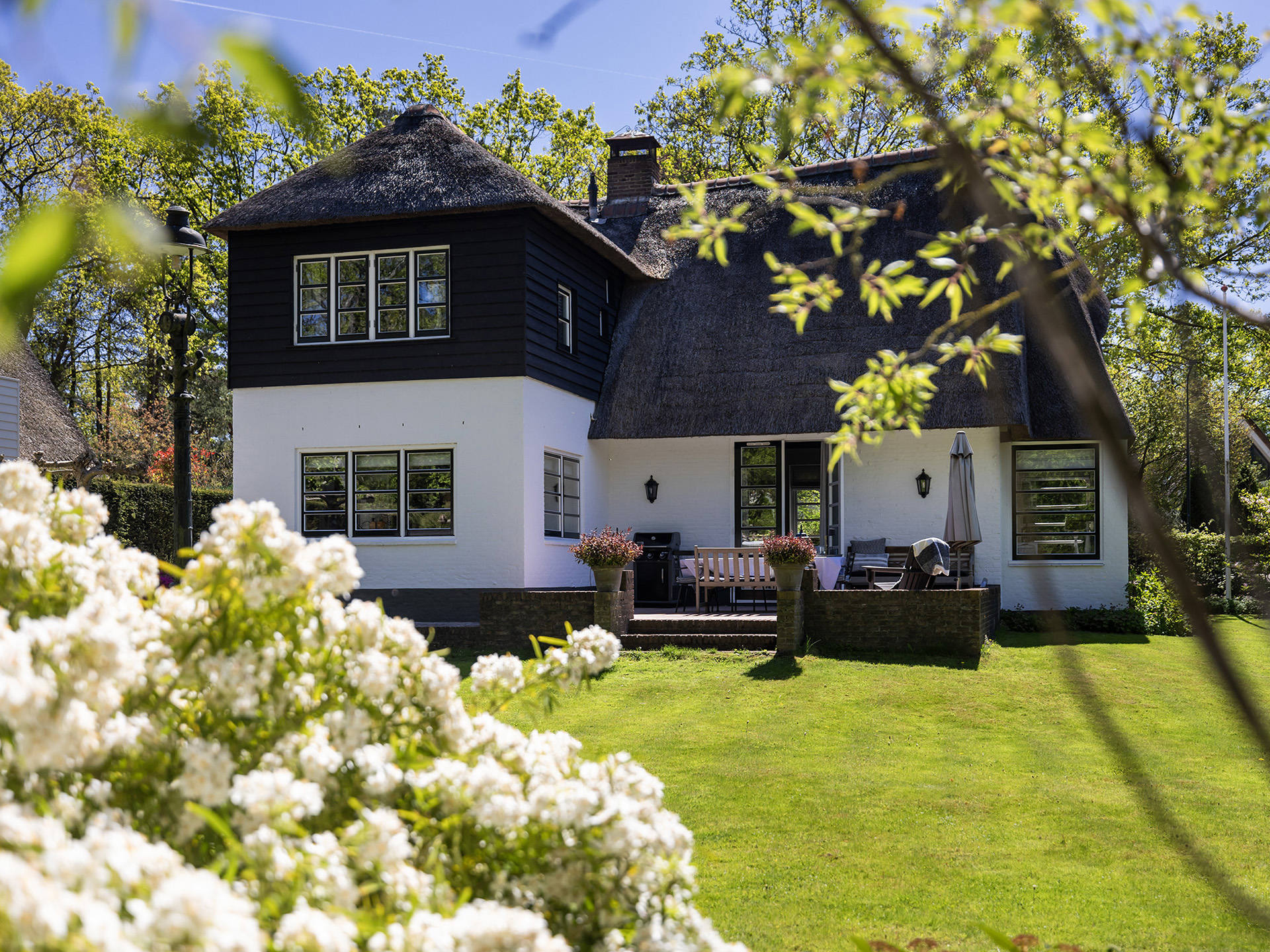 Wit huis met rieten dak, omgeven door een bloeiende tuin in zacht daglicht